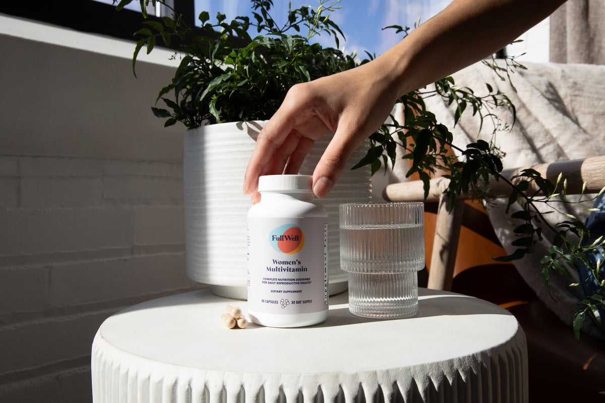 Person holding a supplement bottle on a table with plants in the background